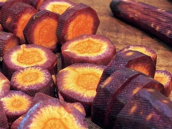 Нарізані шматочки фіолетової моркви з помаранчевою серцевиною на дерев'яній поверхні. - КАРАМЕЛЬ ФІОЛЕТОВА